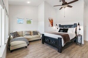 A bedroom with a bed, a sofa, a ceiling fan, and two windows.