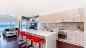 Een moderne keuken met een bar, houten kasten en een groot keukenblok met rode barkrukken.