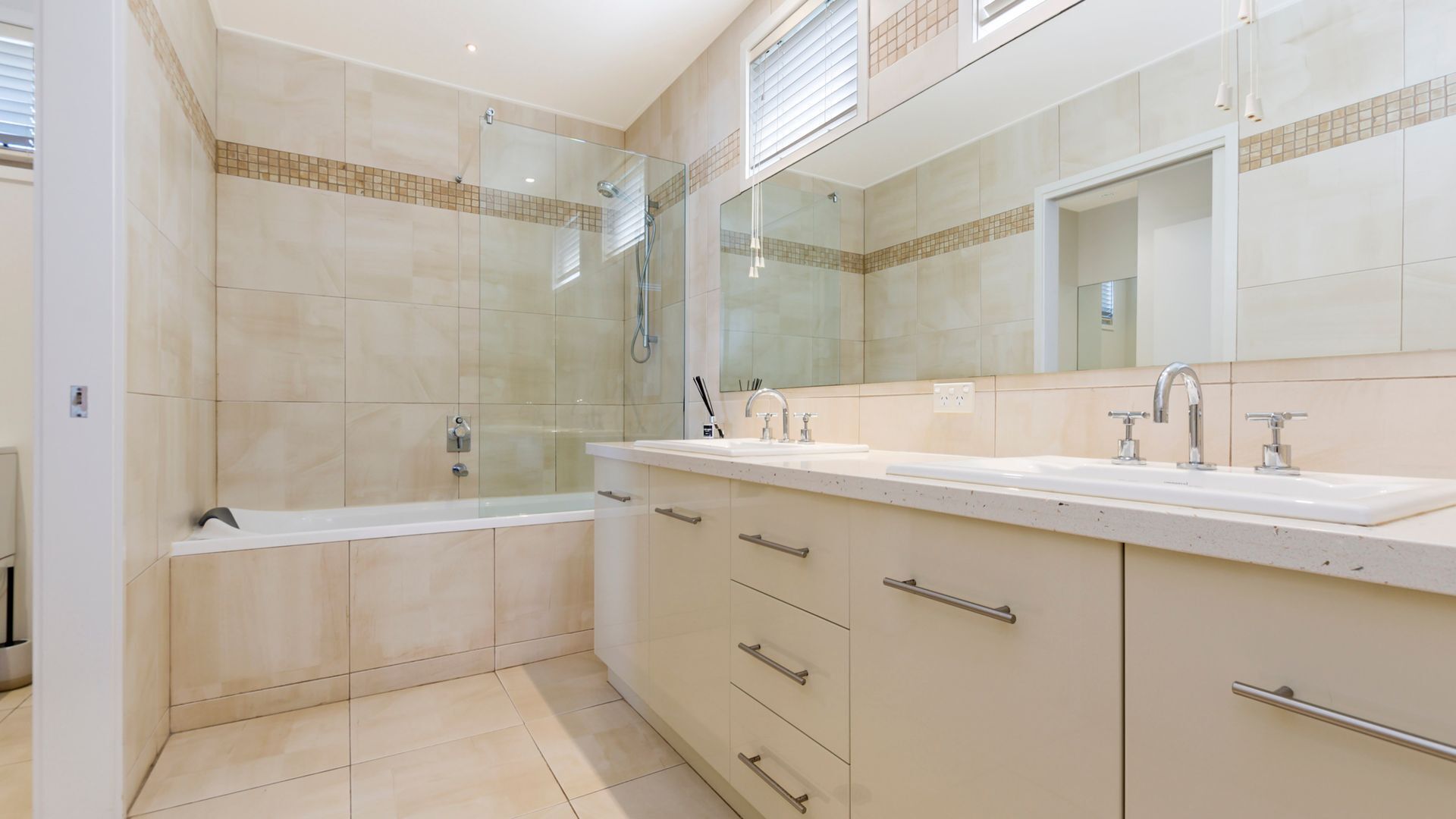 Un baño moderno con ducha de vidrio, un espejo grande y un tocador con lavamanos y almacenamiento.