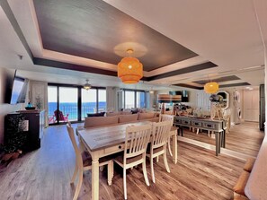 Uma sala de estar ampla com uma grande mesa de jantar de madeira, assentos confortáveis e vista para o oceano.