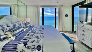 Un dormitorio con cama, cómoda, ventilador de techo y un amplio ventanal con vista al océano.