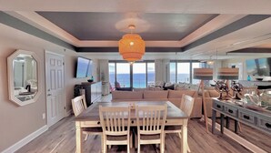 Amplia sala de estar con un sofá grande, una mesa de comedor y sillas, televisor y vista al océano.