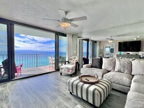 Een ruime woonkamer met een grote bank, een poef en uitzicht op de oceaan.