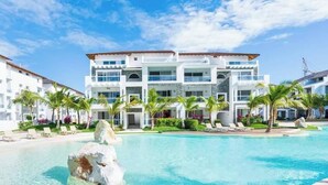 A multi-story hotel with a pool, palm trees, and a clear sky.