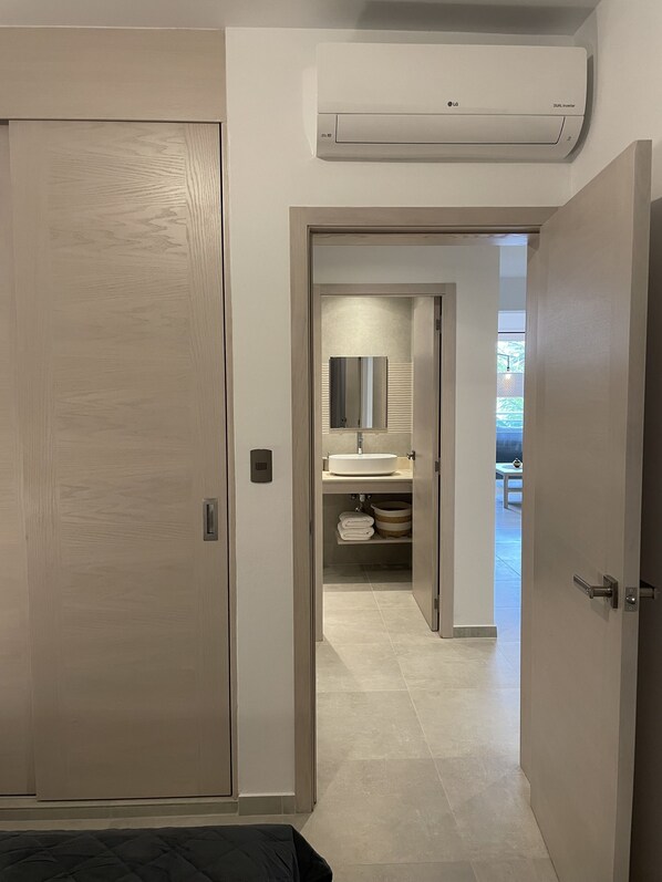 A hotel room with a wooden door, an air conditioning unit, a bathroom with a sink and mirror, and a view of a balcony. - Estrella Dominicus - Hydra203 (San Rafael del Yuma)