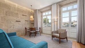 A modern living room with a stone wall, a blue sofa, a wooden chair, a dining table with chairs, and large windows with curtains. - Porta Nobre Boutique Hotel by Aspasios (Porto)