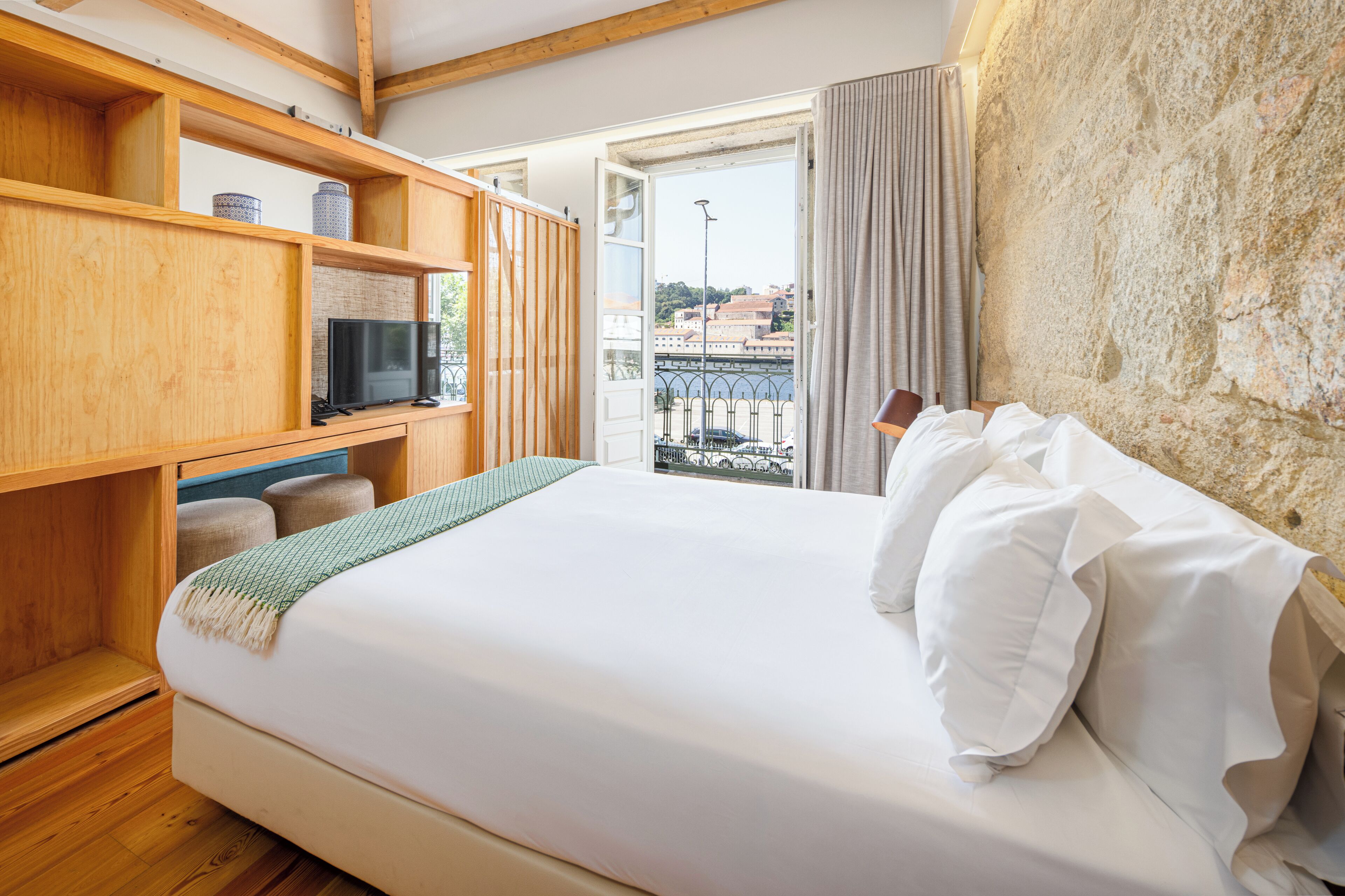 Une chambre d’hôtel avec un lit, des étagères en bois, une télévision et une vue sur un pont et des immeubles.