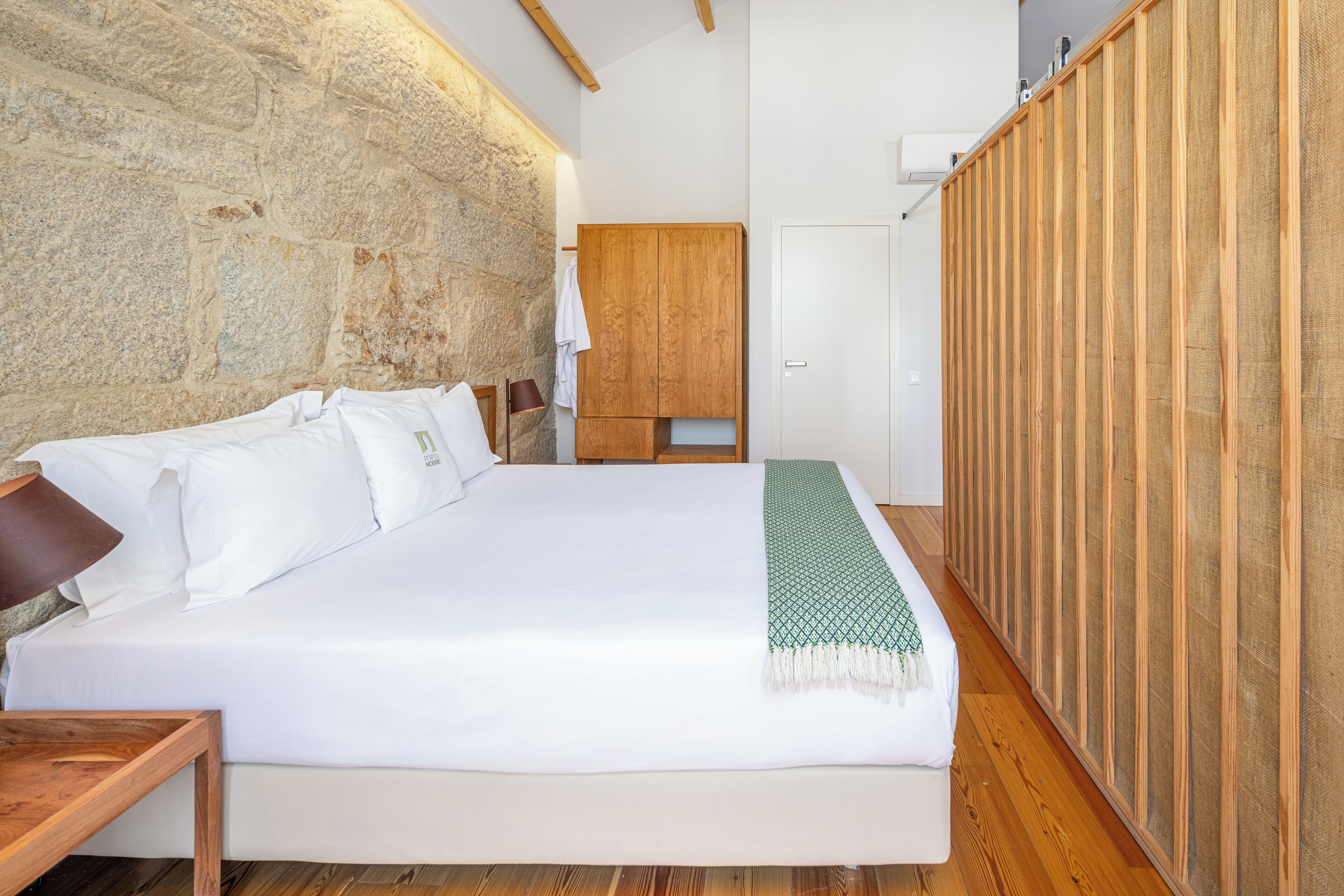 A bedroom with a large bed, wooden wardrobe, stone wall, and a wooden floor.