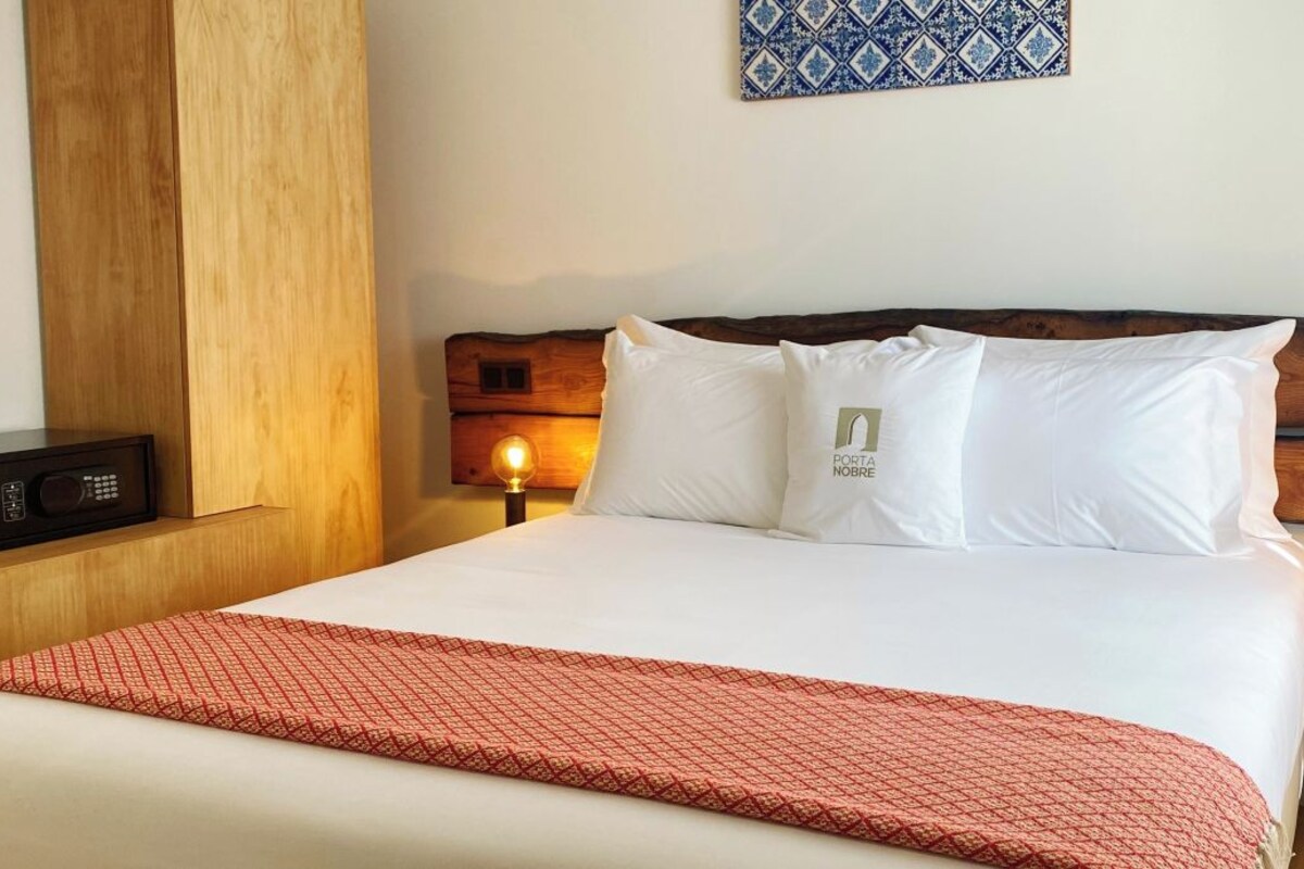 A neatly made bed with a red patterned throw, two bedside lamps, and a wooden nightstand with a radio.