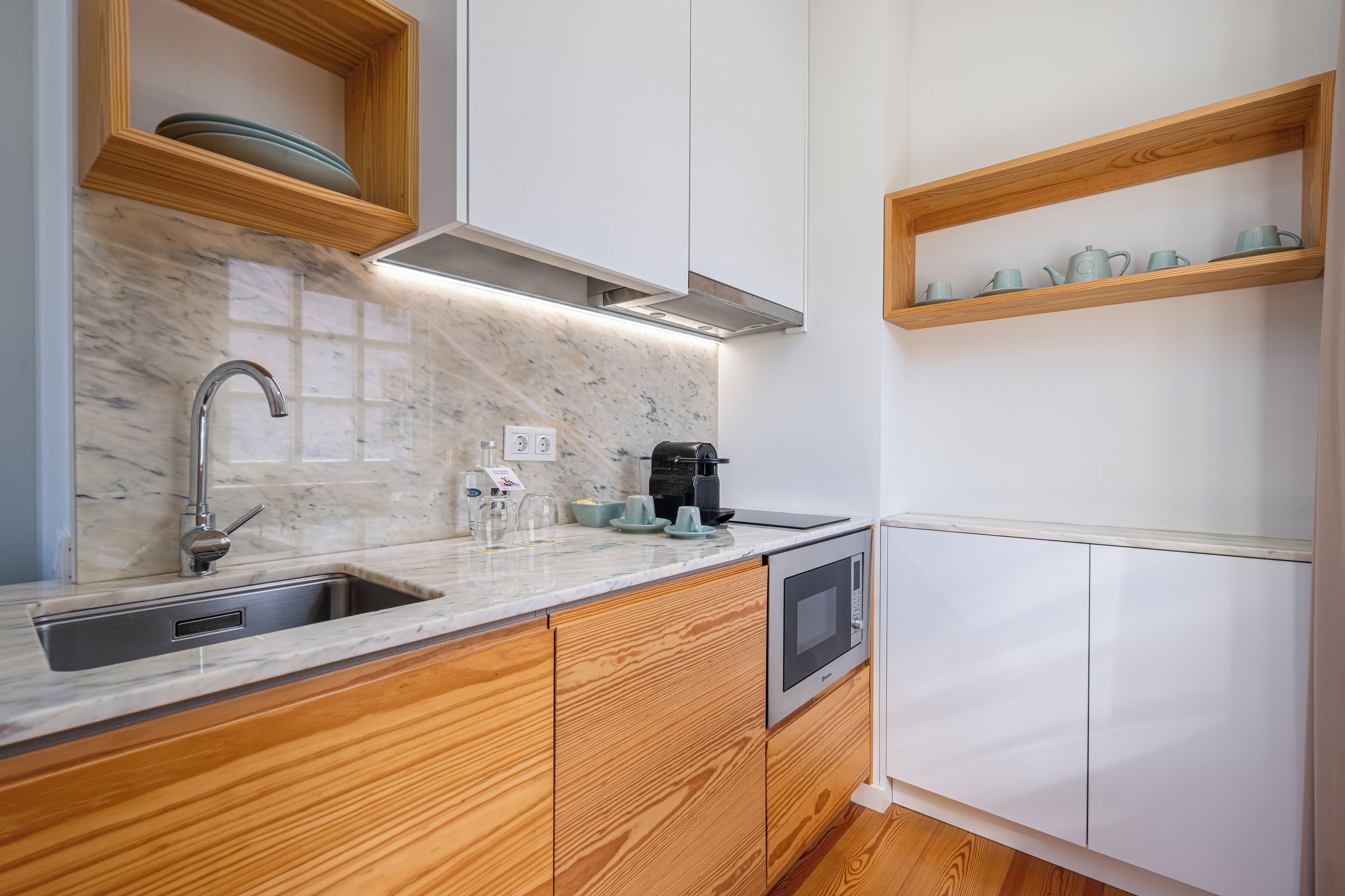 Una cocina moderna con armarios de madera, encimera de mármol, horno empotrado y cafetera.