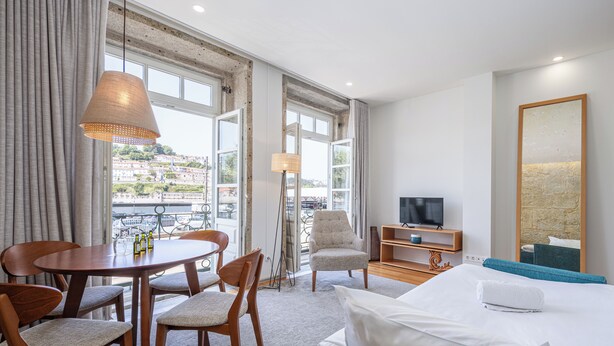 A hotel room with a bed, a TV, a dining table with chairs, and a view of the city. - Porta Nobre Boutique Hotel by Aspasios (Porto)