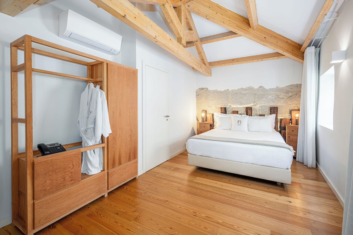 A bedroom with a wooden wardrobe, a bed, and a stone wall.