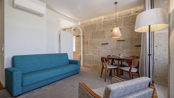 Quarto com sofá azul, mesa de jantar com cadeiras, luminária e parede de pedra.