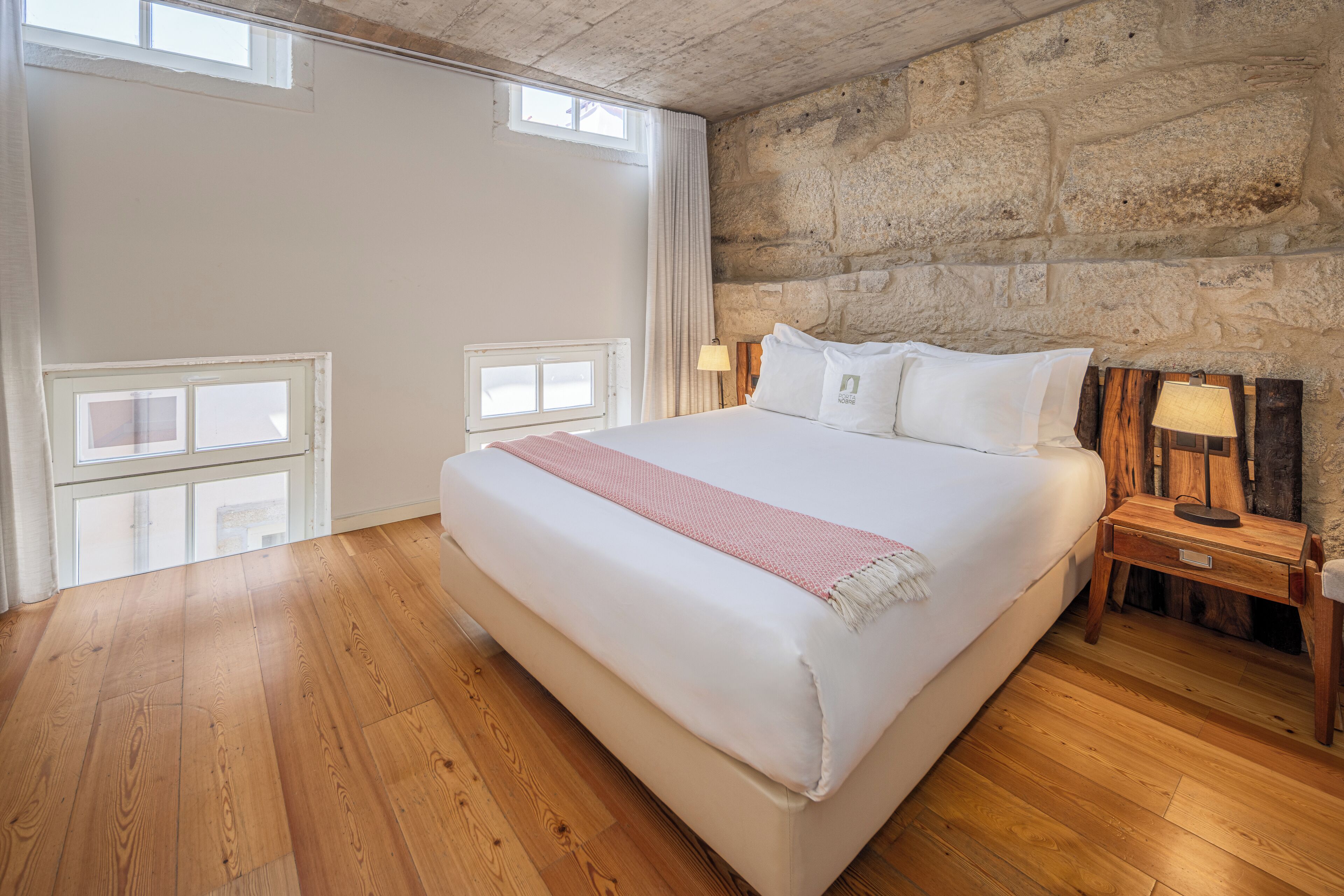 A bedroom with a large bed, wooden floor, stone wall, and two bedside lamps.