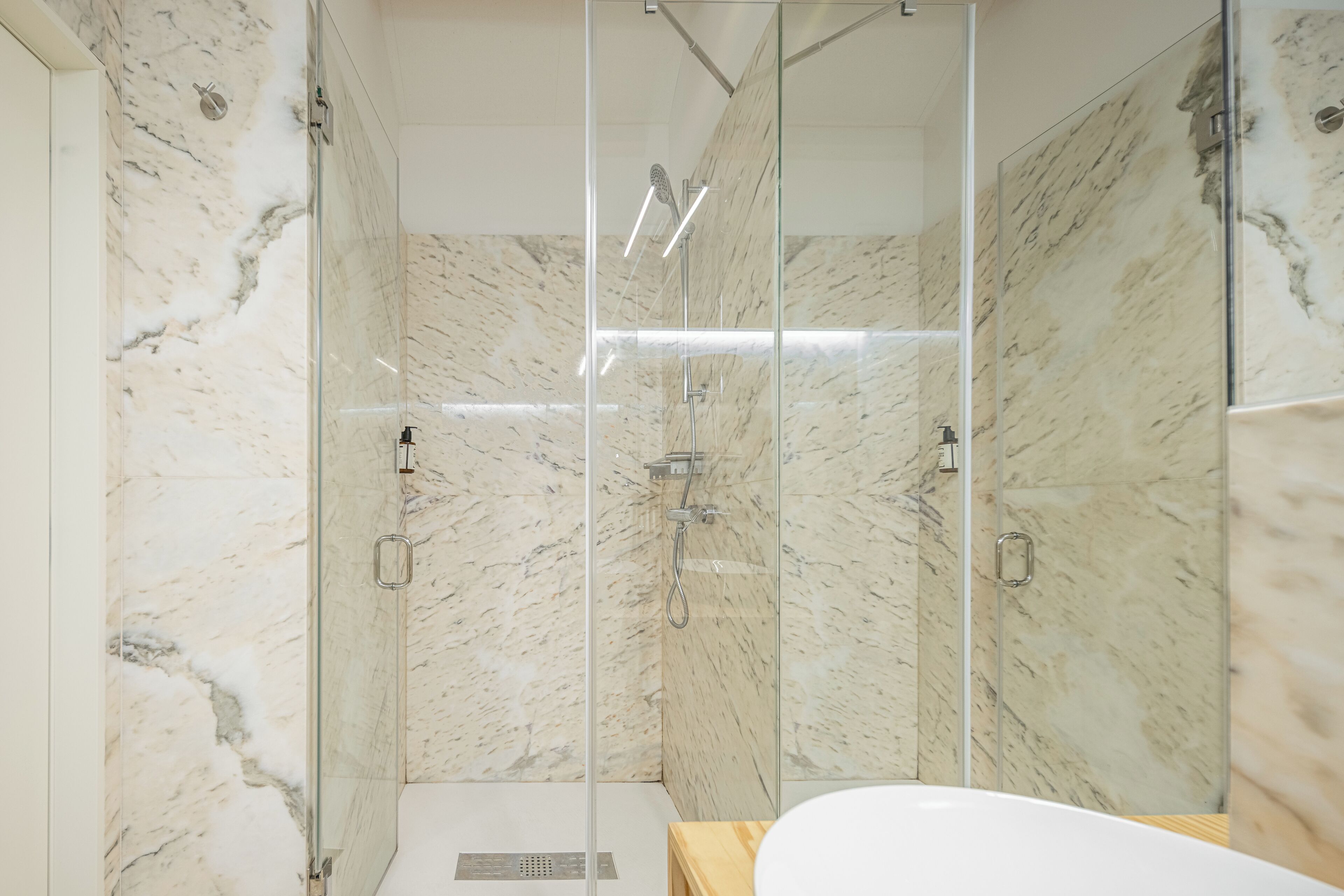 A modern bathroom with a glass-enclosed shower, marble walls, and a wooden vanity.