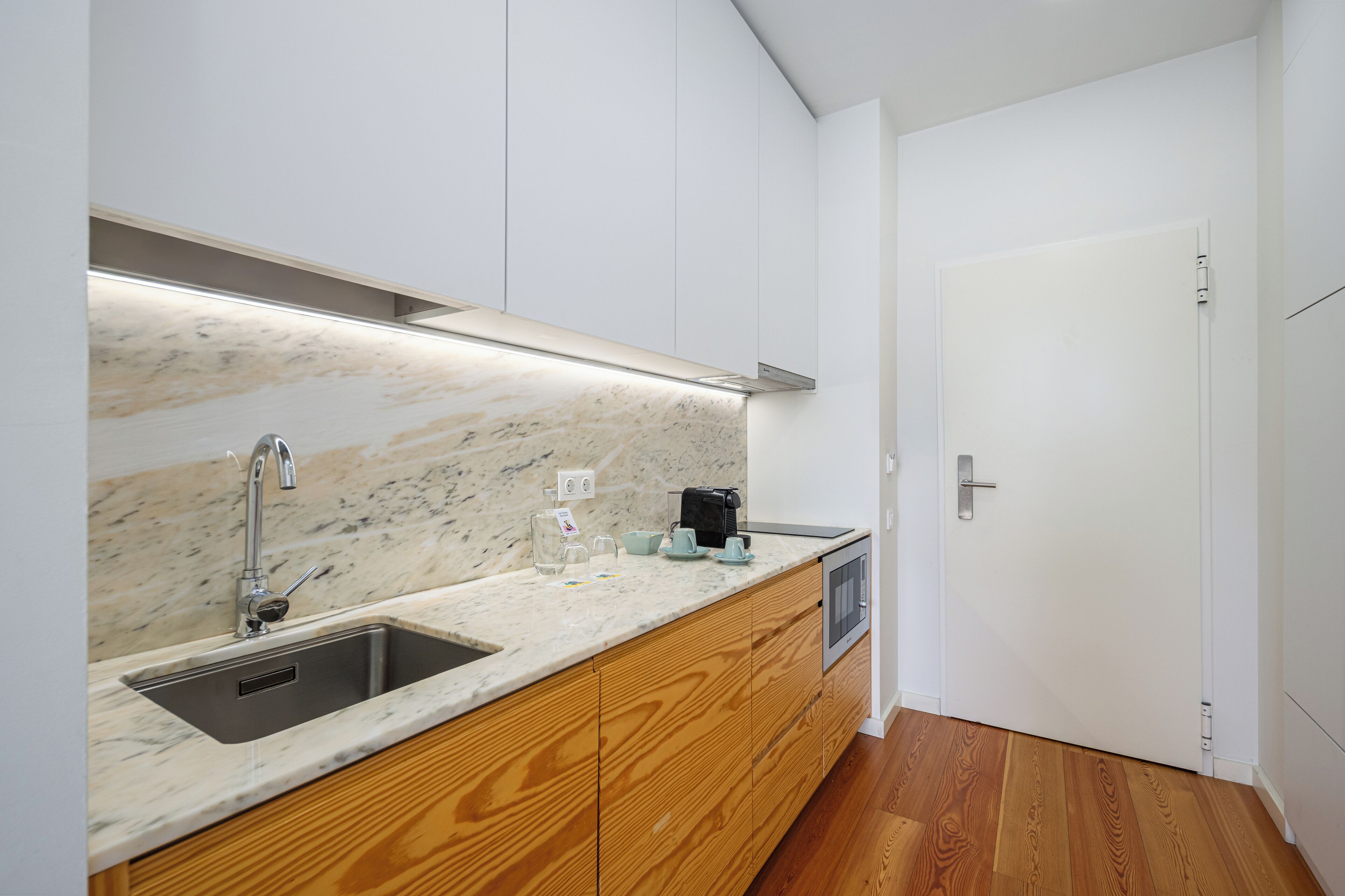 A modern kitchen with a marble countertop, wooden cabinets, a built-in sink, and a coffee maker.