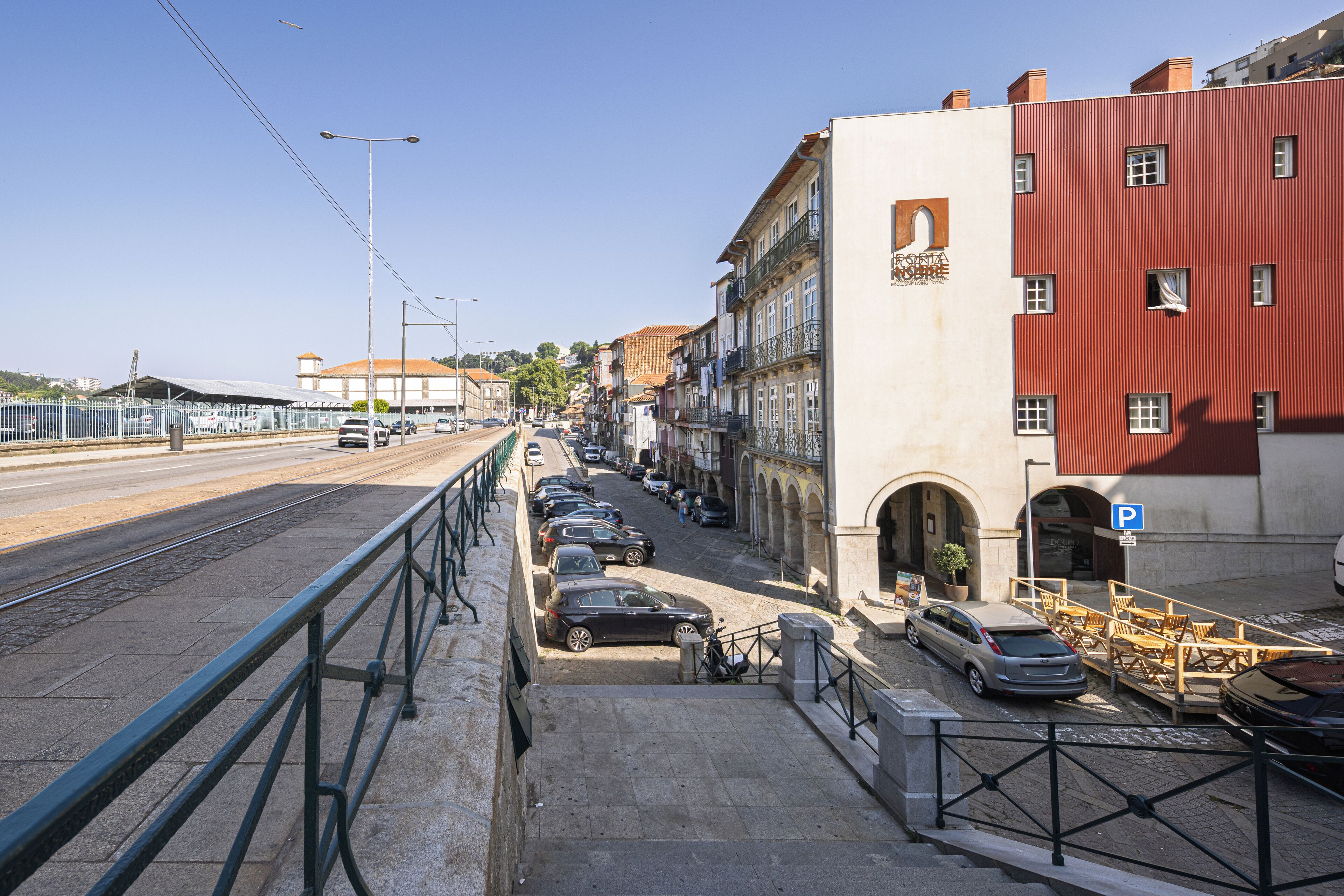 A street view with a tram line, parked cars, and buildings with balconies.