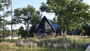 Een chalet met een puntdak, houten terras en uitzicht op een meer.