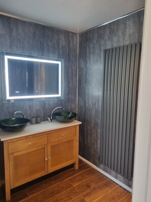 A bathroom with a wooden vanity, two sinks, and a large mirror with integrated lighting. - Stunning 1 Bedroom Lodge (Welshpool)