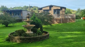 A modern house with a well-maintained lawn and a stone fountain. - Stunning 1 Bedroom Lodge (Welshpool)