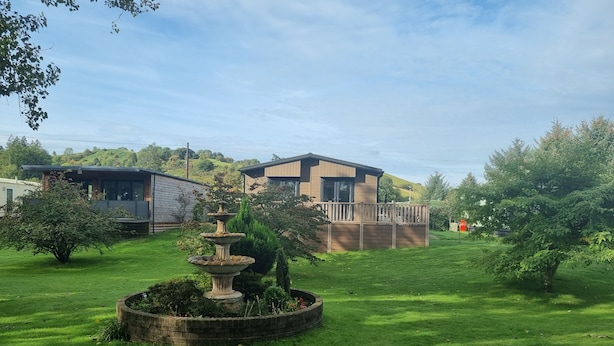 A residential area with two modern houses, a well-maintained lawn, and a central garden with a fountain. - Stunning 1 Bedroom Lodge (Welshpool)