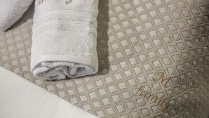 A neatly folded white towel with the word "family" embroidered in gold, placed on a textured beige fabric. - Del Sol Meteora Luxurious Family Suites3 (Kalabaka)