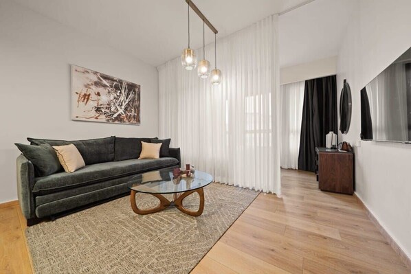 A modern living room with a dark green sofa, a glass coffee table, and a large abstract painting on the wall.