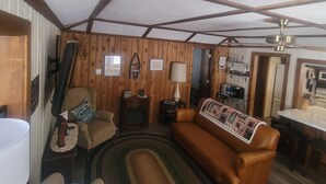 A cozy living room with wooden walls and a ceiling with exposed beams. There is a brown leather sofa, a small table, and a fireplace. - Four season fun, classic LAKEFRONT cabin for families! (Bigfork)