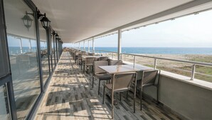 A sunlit deck with tables and chairs, large windows, and a view of the sea. - YALIKÖY DENİZ OTEL (Catalca)