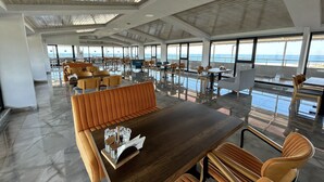 A spacious indoor area with a wooden ceiling, large windows offering a view of the sea, and a variety of seating arrangements including tables and chairs. - YALIKÖY DENİZ OTEL (Catalca)
