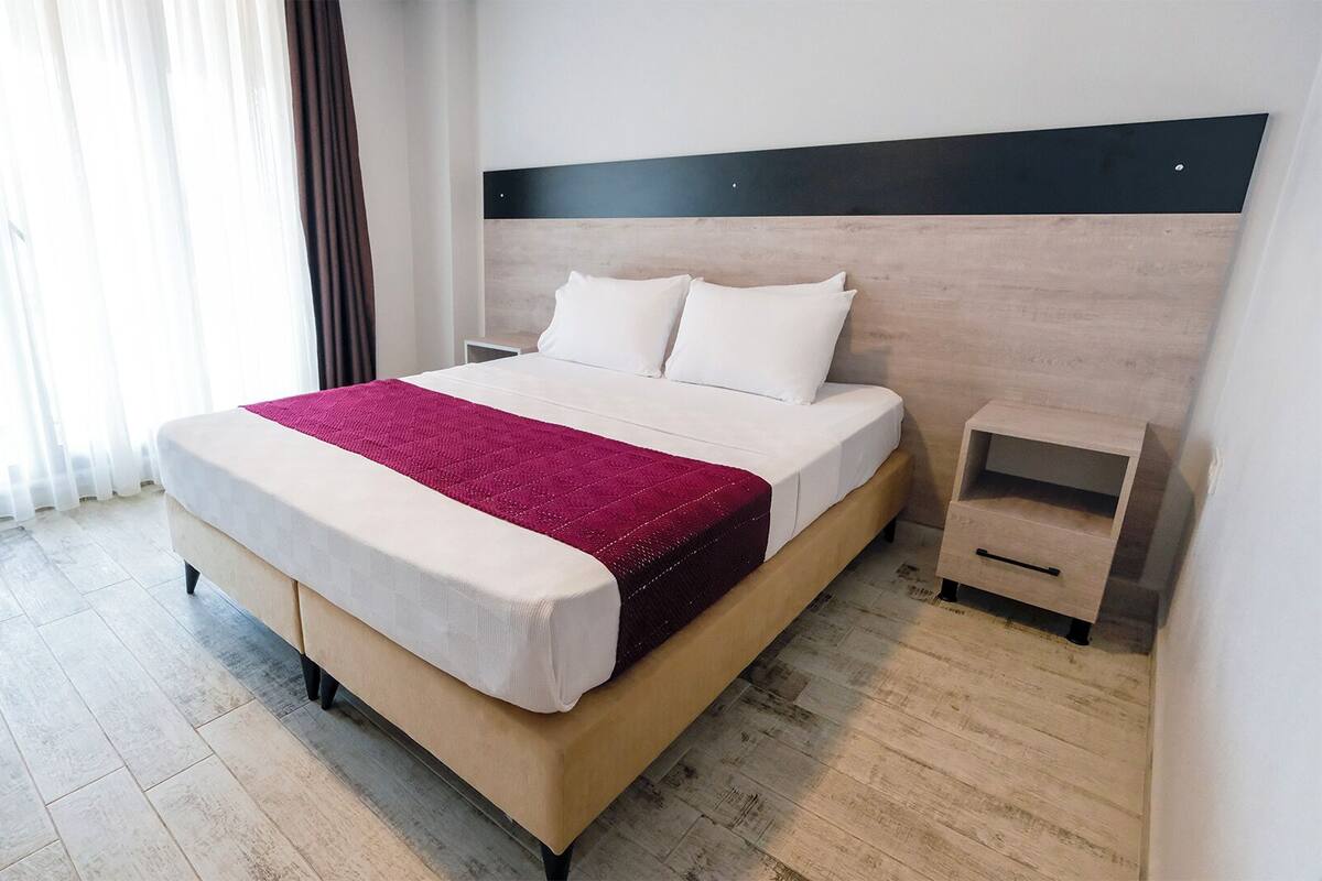 A modern hotel room with a large bed, a bedside table, and a nightstand.