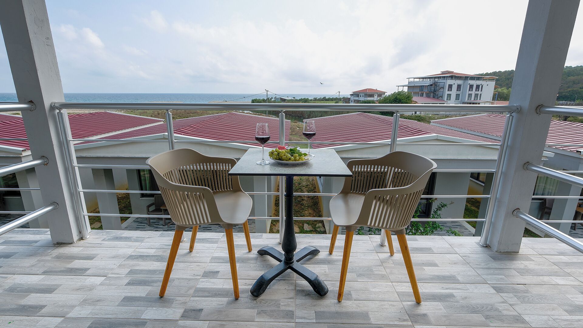A balcony with a table and chairs, overlooking a coastal area with buildings and a view of the sea.