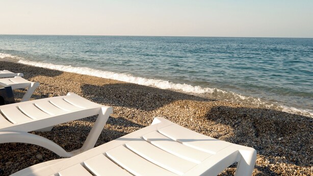 A beach with white lounge chairs and pebbles. - YALIKÖY DENİZ OTEL (Catalca)