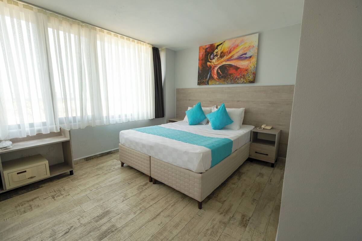 A bedroom with a bed, bedside tables, a desk, and a painting on the wall.