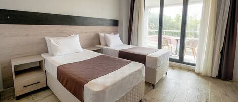 A hotel room with two beds, a wooden headboard, a sliding glass door to the balcony, and a small wooden nightstand.