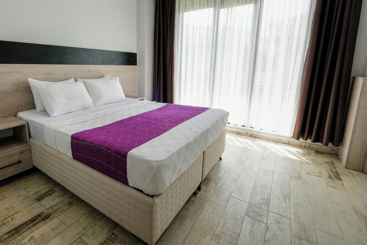A hotel room with a bed, a nightstand, and a window with curtains.