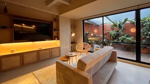 A modern living room with a large TV, comfortable seating, and a view of the outdoor garden. - w* | Charming 1BR Apartment w/ Terrace in Laureles (Medellín)