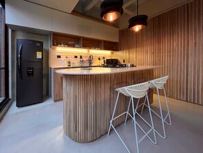Een moderne keuken met een centraal eiland, twee barkrukken, een koelkast en houten lambrisering.