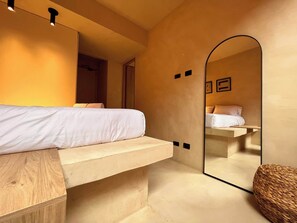 Een moderne slaapkamer met een bed, een houten bankje, een grote spiegel en een geweven mand.