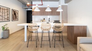 A modern kitchen with a central island, three wicker bar stools, pendant lights, and a potted plant.