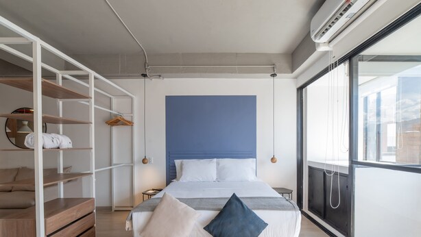 A modern bedroom with a large bed, built-in shelving, a bedside table, and a view through a large window.