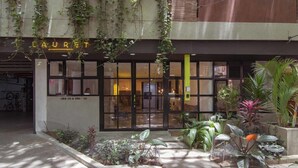A building with a sign reading "LAURET" and a glass entrance. There are plants and a small garden area in front.