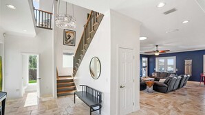 A spacious living area with a staircase, a bench, a sofa, and a ceiling fan. - Waterfront Home w Patio, Heated Pool, Dock, Beach (St. Augustine)