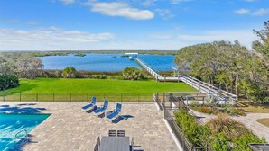A pool area with lounge chairs and a view of the water. - Waterfront Home w Patio, Heated Pool, Dock, Beach (St. Augustine)