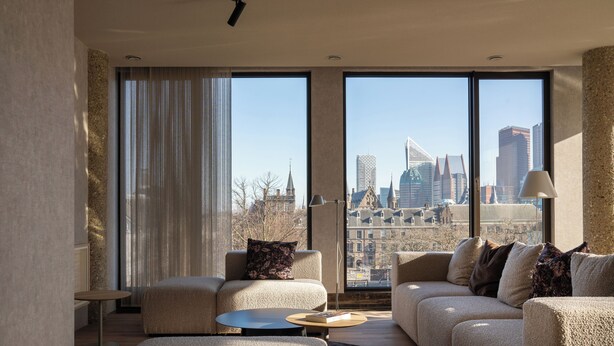 Ein modernes Wohnzimmer mit großem Fenster und Blick auf die Stadt, einem runden Couchtisch und einer Couch mit Zierkissen.