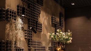 Ein modernes Interieur mit strukturierter Wand, einer Pendelleuchte und einer Vase mit Blumen.