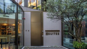 Ein modernes Gebäude mit Glastür, einem Schild mit der Aufschrift 'Suites' und einem Blumentopf mit einem Baum.