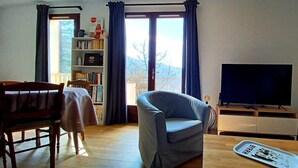 A living room with a sofa, a dining table with chairs, a bookshelf, and a television. - The Isard appt (Vernet-les-Bains)