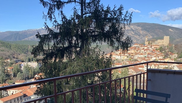 A balcony with a round table and chairs, overlooking a town with a castle and mountains in the background. - The Isard appt (Vernet-les-Bains)