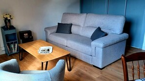 A living room with a grey sofa, a wooden coffee table, a blue armchair, and a small bookshelf with a vase of flowers. - The Isard appt (Vernet-les-Bains)